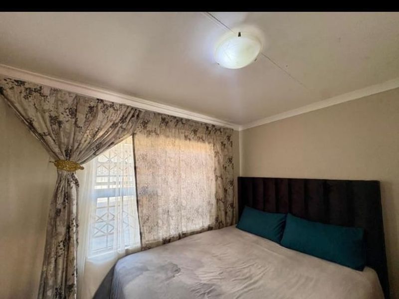 A bedroom featuring a window with security bars and a central ceiling light fixture.