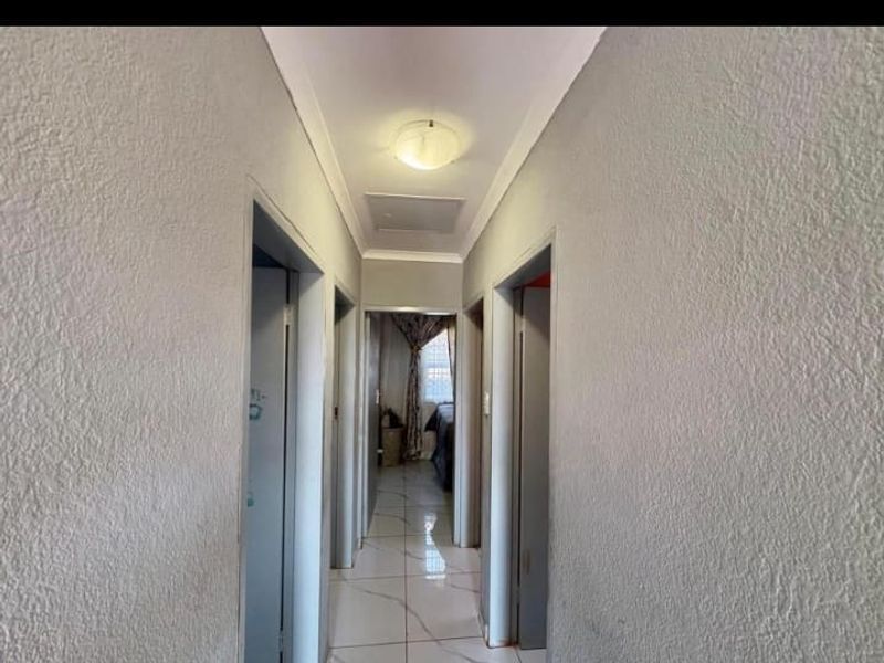 A simple interior hallway featuring tiled flooring and a central ceiling light fixture, providing access to adjacent rooms.