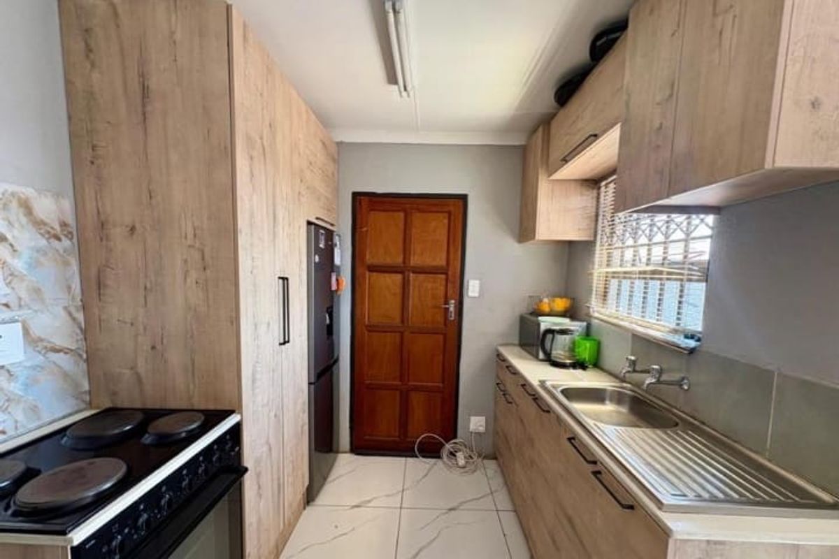 A functional kitchen featuring wood-look cabinetry, a stainless steel sink, and an electric stove with tiled flooring.