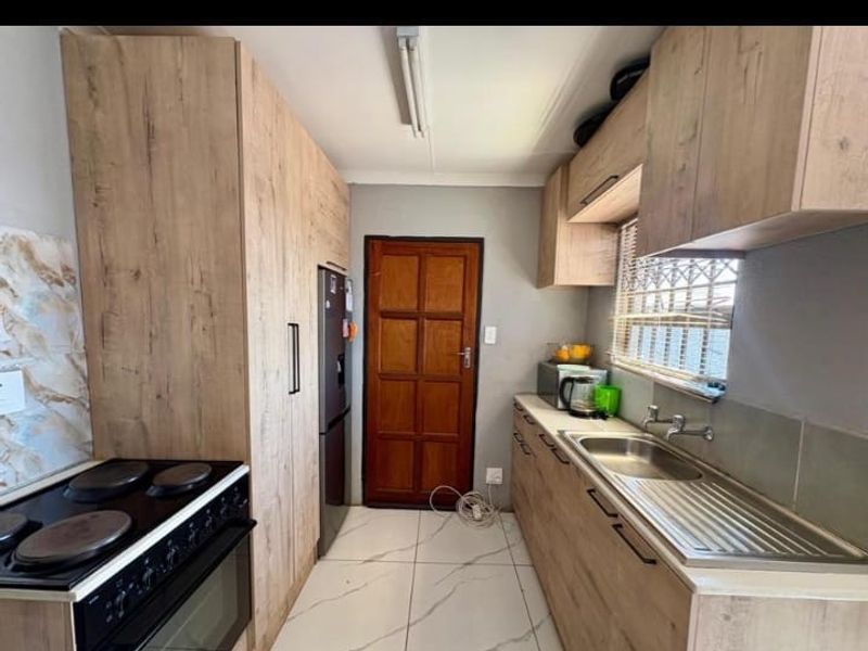 A functional kitchen featuring wood-look cabinetry, a stainless steel sink, and an electric stove with tiled flooring.