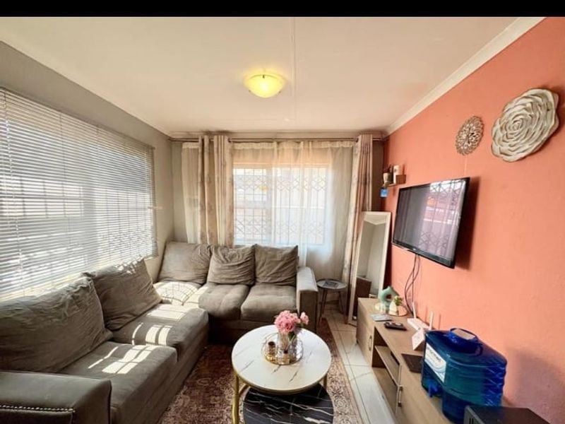A compact living room featuring tiled flooring, venetian blinds, and a feature wall, providing a functional and cozy space.