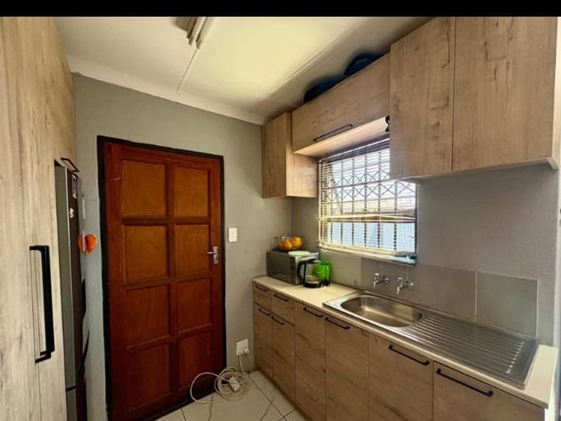A compact kitchen featuring wood-look cabinetry, a stainless steel sink, and tiled flooring, providing a functional workspace.