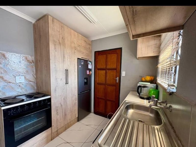 A functional kitchen featuring wood-look cabinetry, a stainless steel sink, and a built-in electric stove and oven with tiled flooring.