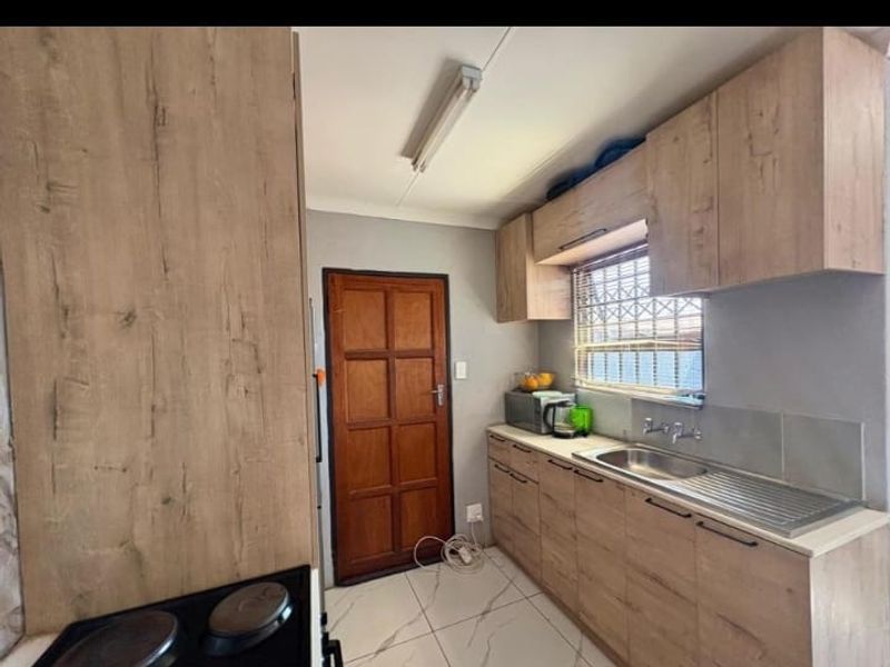 A functional kitchen featuring wood-look cabinetry, a stainless steel sink, tiled flooring, and a built-in hob.