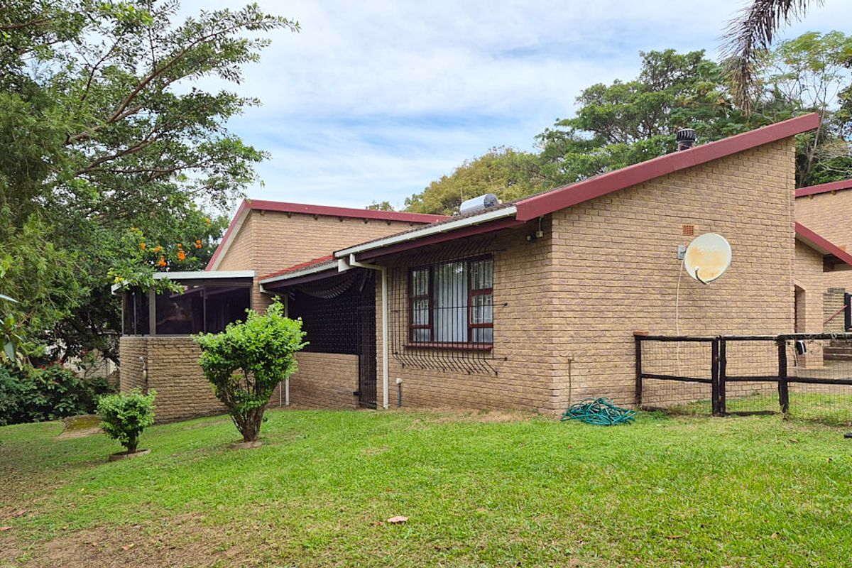 Rear view of a face brick house featuring a pitched roof, security bars on windows, and a spacious garden area.