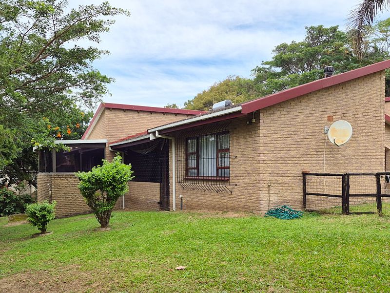 Rear view of a face brick house featuring a pitched roof, security bars on windows, and a spacious garden area.