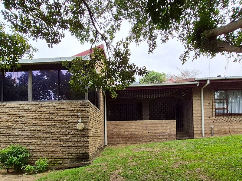 Rear view of a face brick house featuring a covered patio area, security bars on windows, and a sloped garden setting.