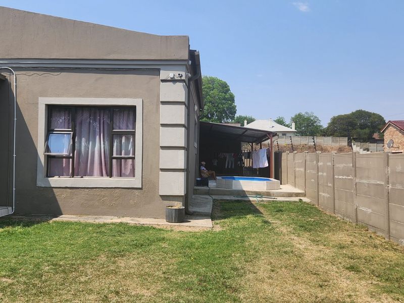 Rear view of the property featuring a small swimming pool, covered patio area, and a precast concrete boundary wall enclosing the garden.