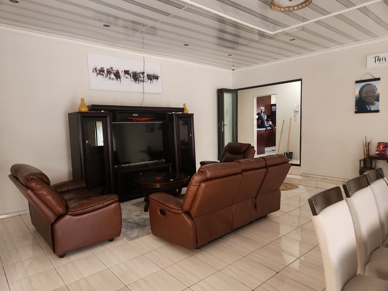A spacious living room featuring tiled flooring, decorative ceiling panels with recessed lighting, and a neutral wall finish.