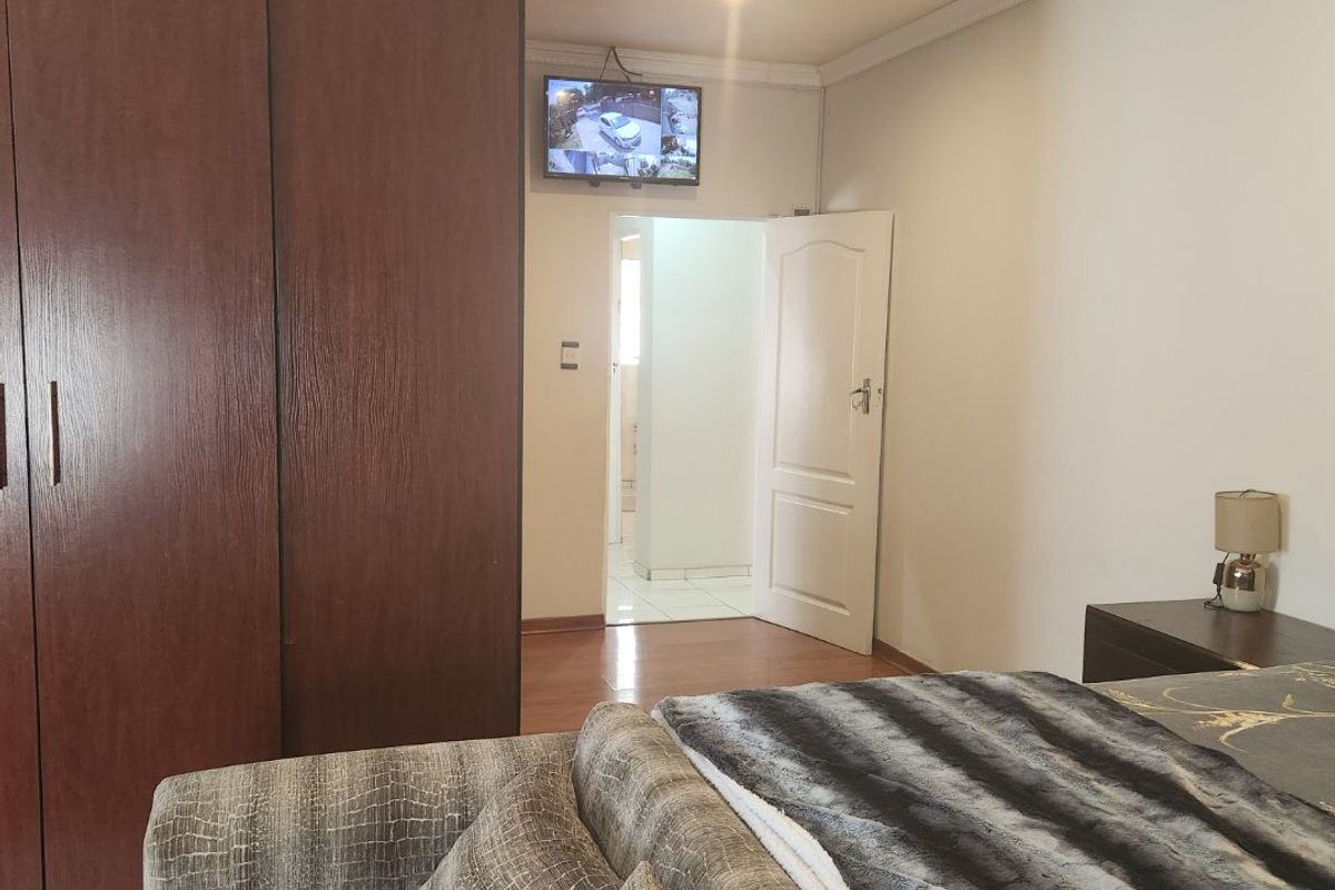 A bedroom featuring dark wood built-in wardrobes, laminate flooring, and decorative ceiling coving, with an adjacent doorway leading to an adjoining room.