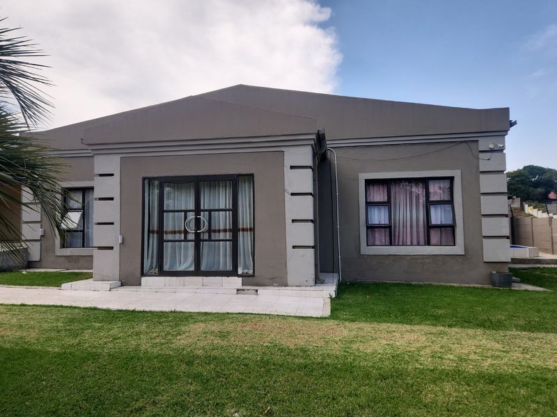 Front elevation of a single-story house featuring a tiled patio, aluminium framed glass sliding doors, and large windows set in a plastered facade.