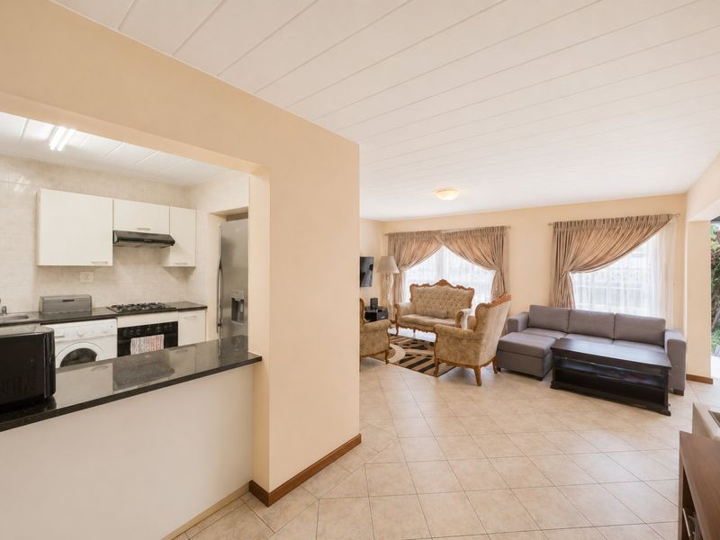 Open-plan living area featuring a functional kitchen with granite countertops, gas hob, and built-in oven, flowing into a spacious lounge with tiled flooring.