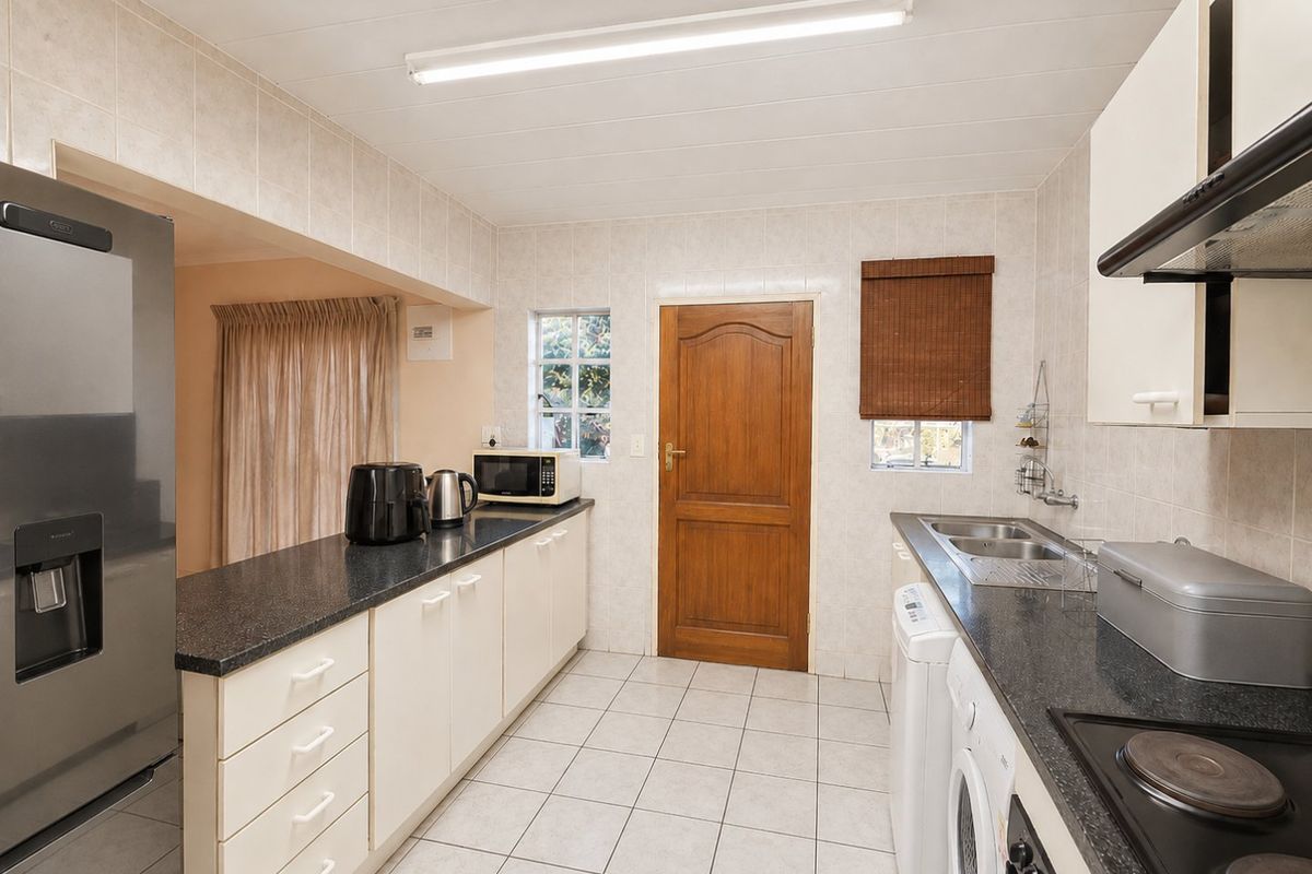 A functional kitchen featuring built-in cabinetry, dark laminate countertops, a double sink, and an electric hob with an extractor fan.