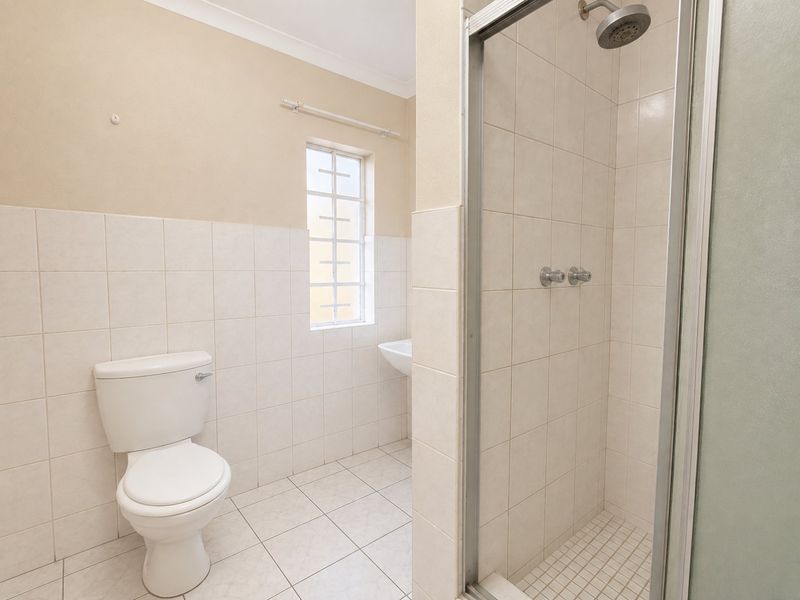 A functional bathroom featuring a shower enclosure, pedestal basin, and toilet, finished with neutral wall and floor tiles.