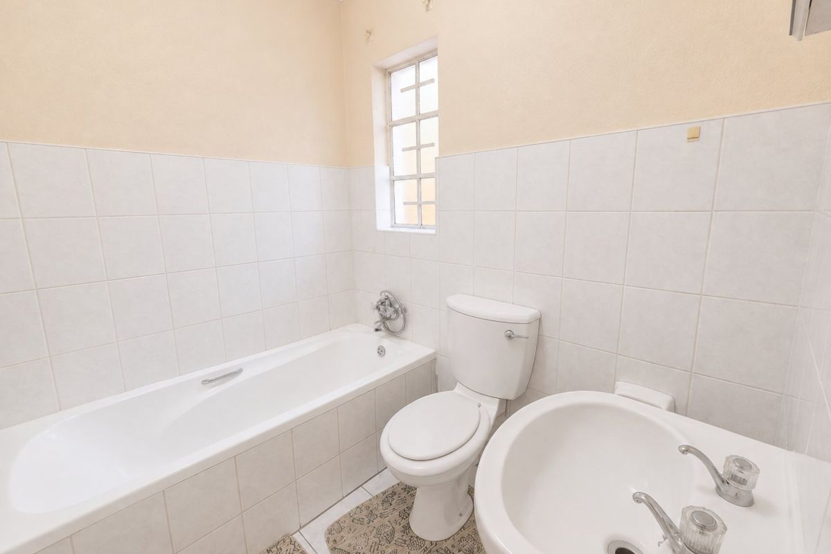 A functional bathroom featuring a standard bathtub, toilet, and pedestal basin with neutral wall tiling and a window for natural light.