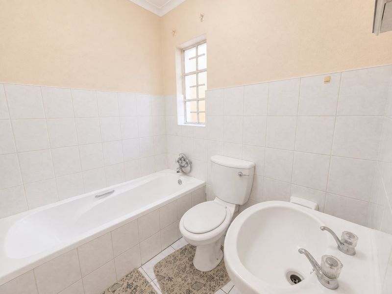 A functional bathroom featuring a standard bathtub, toilet, and pedestal basin with neutral wall tiling and a window for natural light.