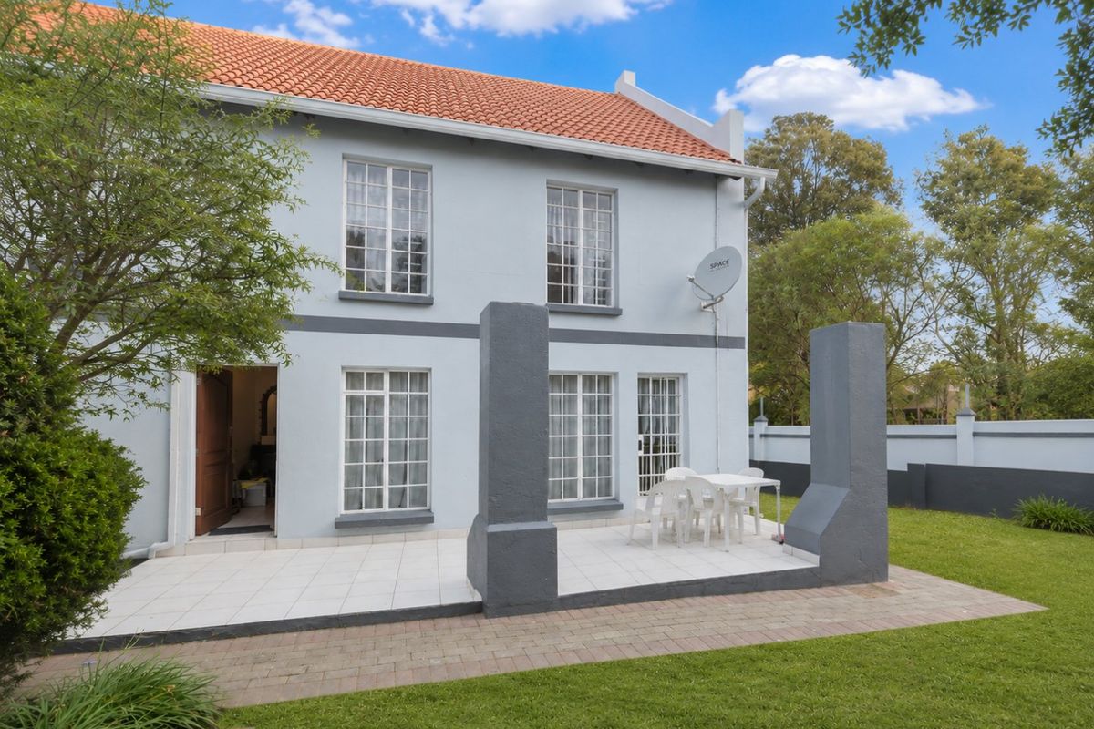 Rear view of the townhouse featuring a tiled patio area, established garden, and classic terracotta roof tiles.