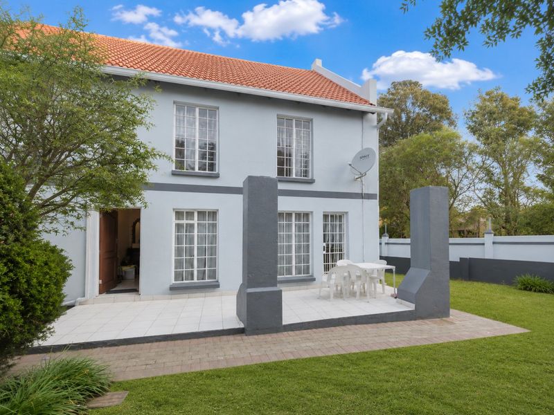 Rear view of the townhouse featuring a tiled patio area, established garden, and classic terracotta roof tiles.