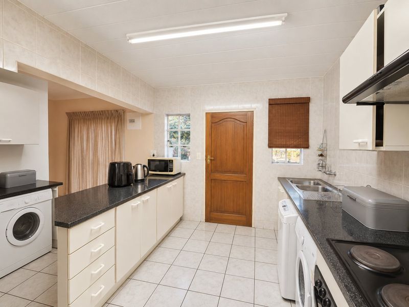 Functional kitchen featuring ample built-in cabinetry, laminate countertops, a double sink, and integrated electric hob with extractor fan, finished with tiled flooring and walls.