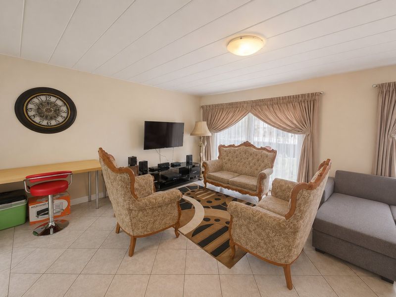 A comfortable living room featuring tiled flooring, panelled ceiling, and a sliding glass door providing natural light.