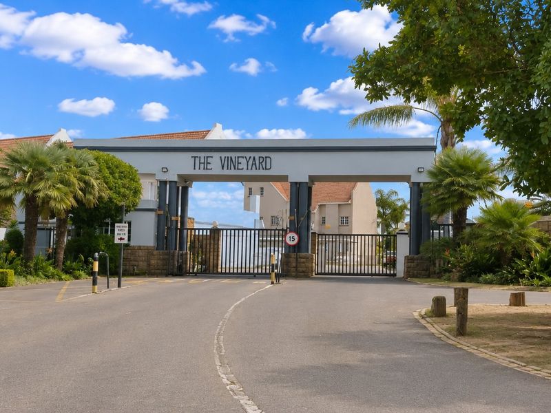 The main entrance gate to The Vineyard residential estate, featuring a secure gated access point, paved driveway, and established landscaped surroundings.