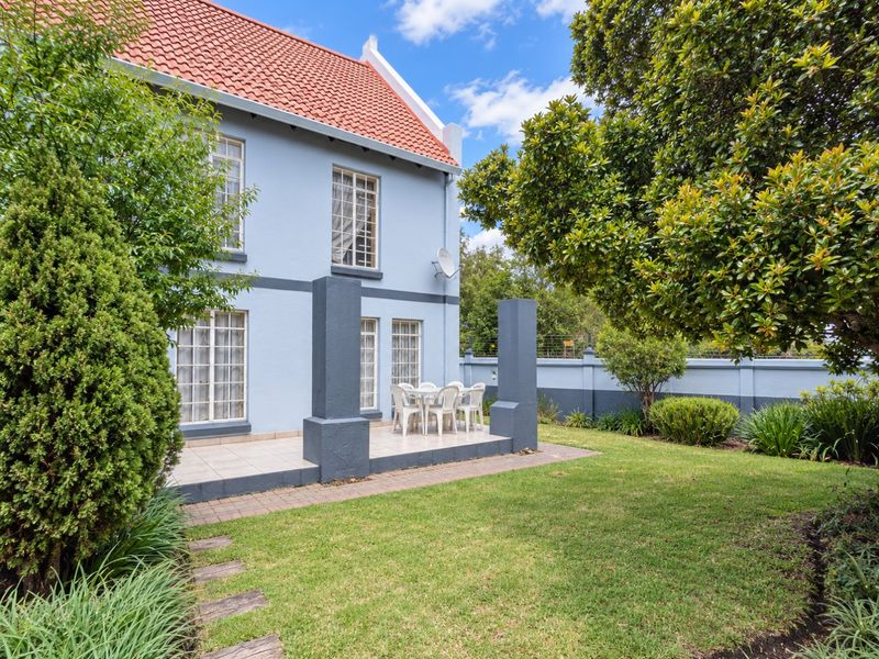 Rear view of the townhouse featuring a tiled patio area, landscaped garden, and a well-maintained exterior facade with terracotta roof tiles.