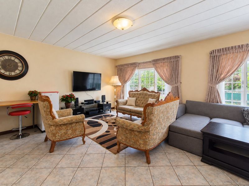 A spacious living room featuring tiled flooring, a panelled ceiling, and large windows that provide ample natural light.