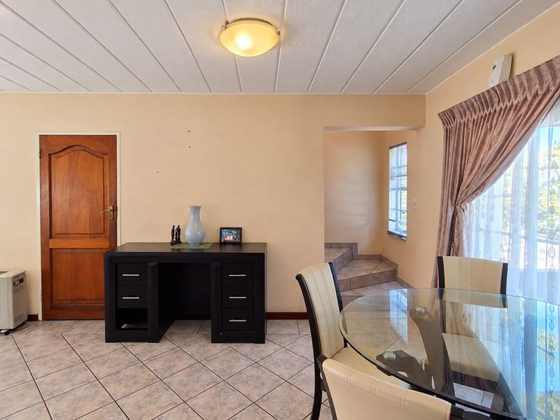 A dining area featuring tiled flooring, a panelled ceiling, and a timber door leading to a tiled staircase.