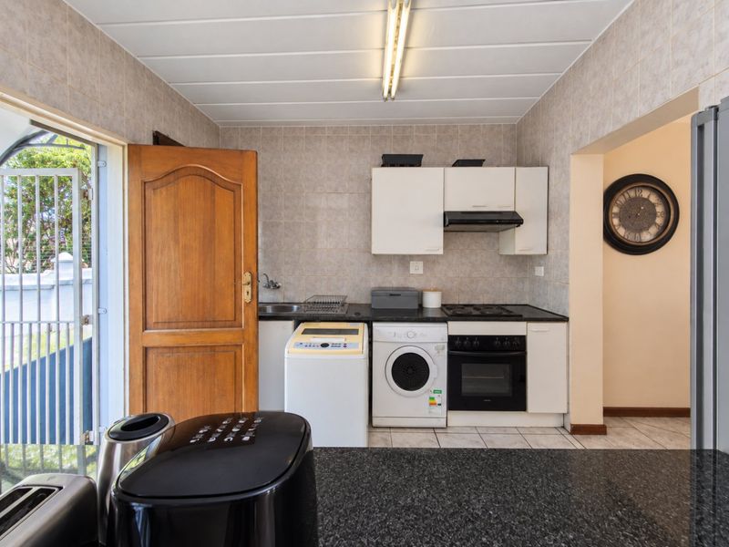 Compact kitchen featuring built-in cabinetry, integrated oven and hob, tiled splashbacks, and direct access to an outdoor area.
