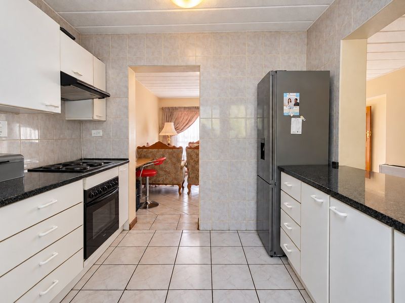 A functional kitchen featuring white cabinetry, granite countertops, tiled walls and flooring, and built-in cooking appliances, with a view into the adjacent living area.