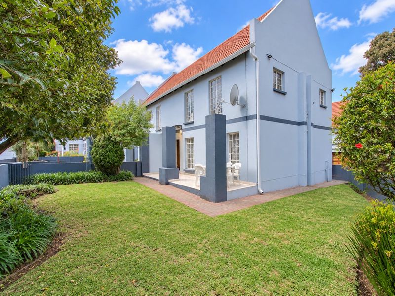 Rear view of the townhouse featuring a paved patio area, well-maintained lawn, and a classic tiled roof structure.