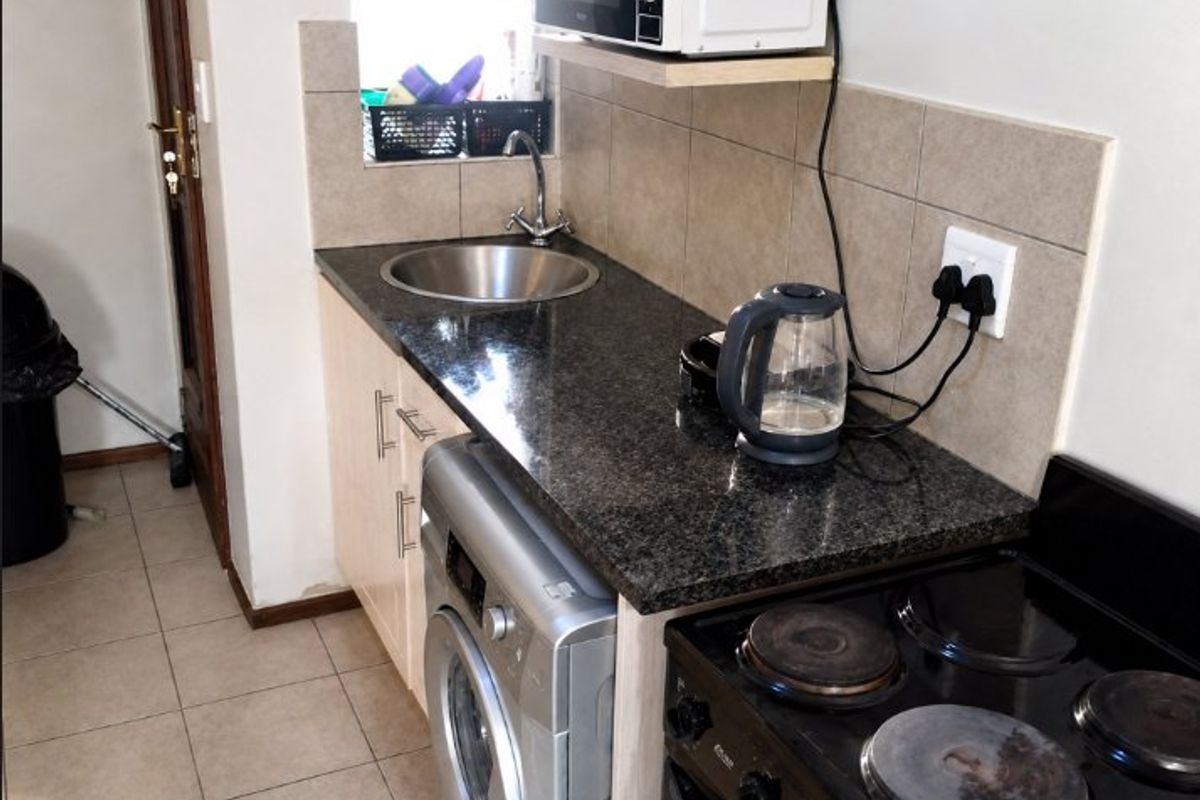 Compact scullery area featuring granite countertops, a stainless steel sink, tiled backsplash, and integrated laundry and cooking facilities.