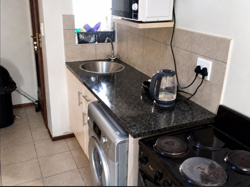 Compact scullery area featuring granite countertops, a stainless steel sink, tiled backsplash, and integrated laundry and cooking facilities.