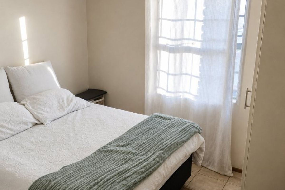 A functional bedroom featuring tiled flooring, a built-in wardrobe, and natural light through a window.
