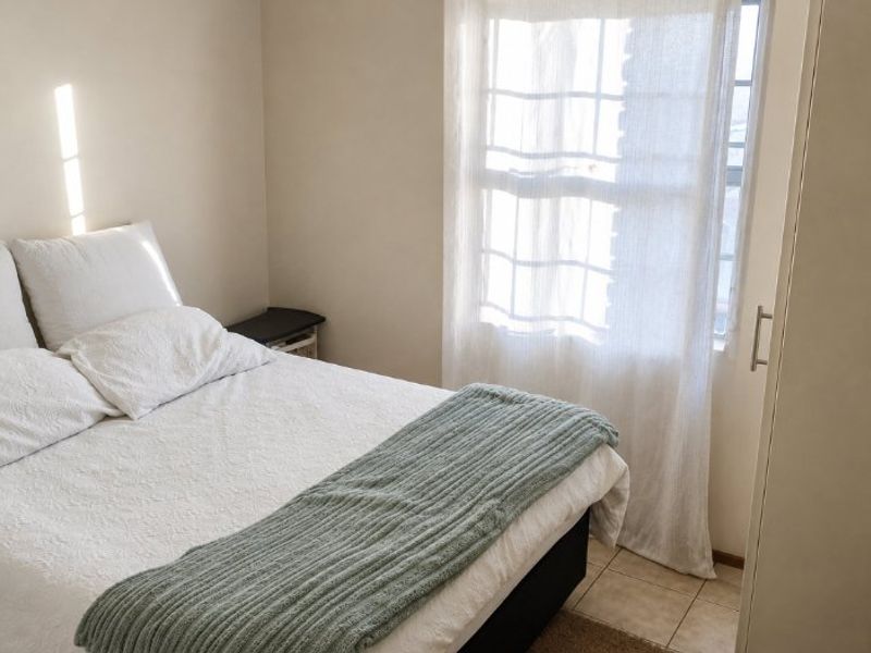 A functional bedroom featuring tiled flooring, a built-in wardrobe, and natural light through a window.