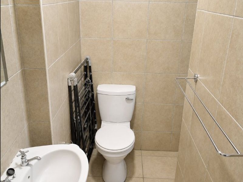 A compact bathroom featuring tiled walls and flooring, equipped with a standard toilet and a pedestal basin.