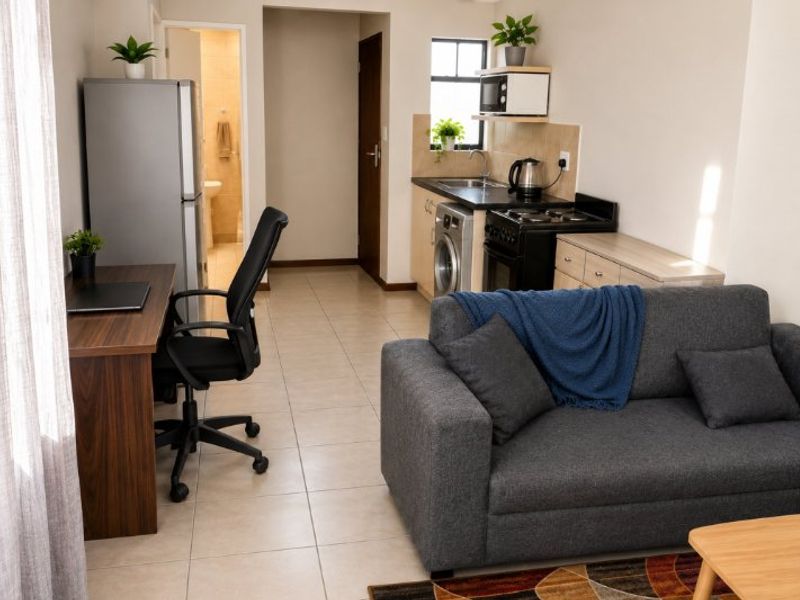 An open-plan living area featuring a compact kitchen with built-in cabinetry, stove, and sink, seamlessly connected to a living and workspace area.