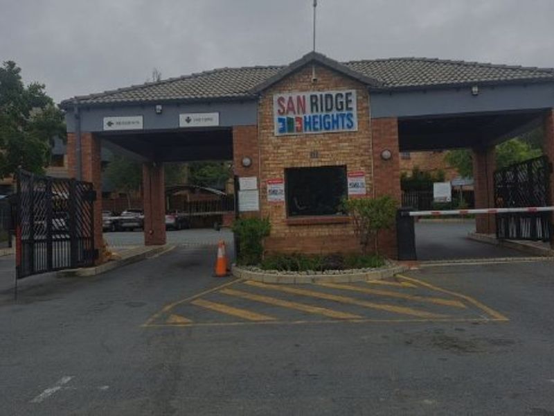 The main entrance and security gatehouse of San Ridge Heights, featuring a brick facade, boom gates, and controlled access point.