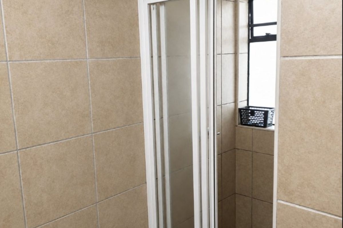 A functional bathroom shower area featuring tiled walls and a white framed shower enclosure with an adjacent window.