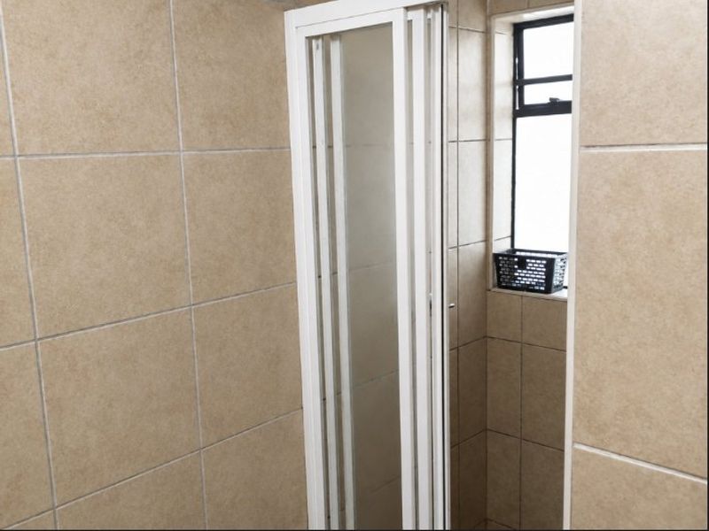 A functional bathroom shower area featuring tiled walls and a white framed shower enclosure with an adjacent window.