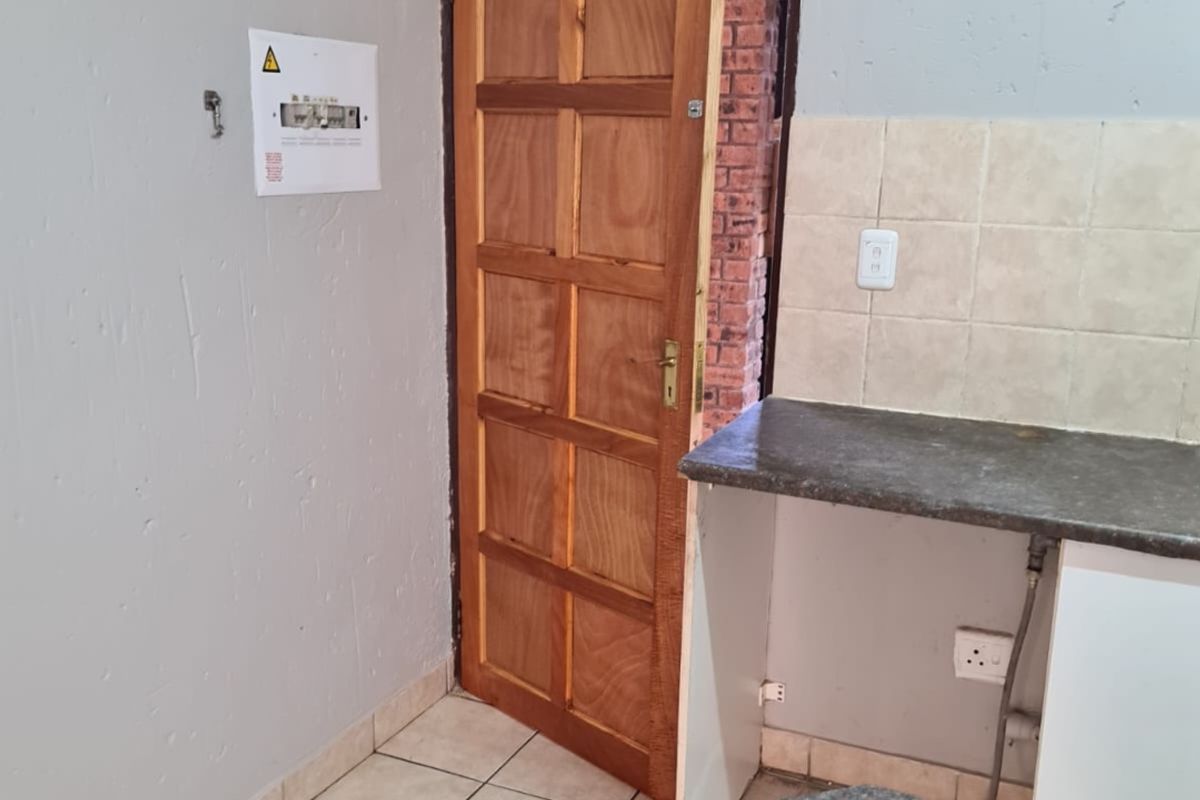 A functional kitchen area featuring tiled flooring, laminate countertops, and a tiled backsplash, with an integrated electrical distribution board.