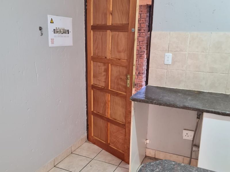 A functional kitchen area featuring tiled flooring, laminate countertops, and a tiled backsplash, with an integrated electrical distribution board.
