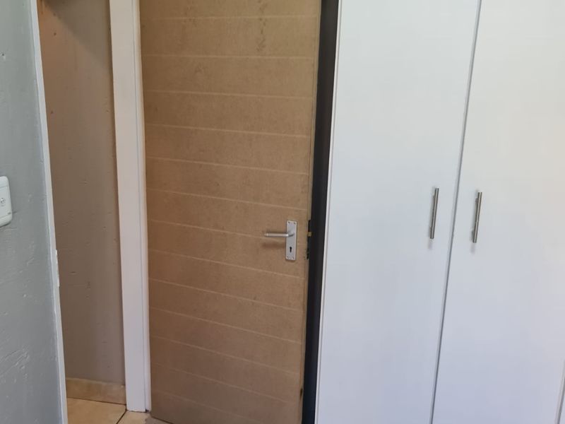 A bedroom interior featuring a built-in wardrobe and an unfinished wooden door leading to an adjacent space with tiled flooring.