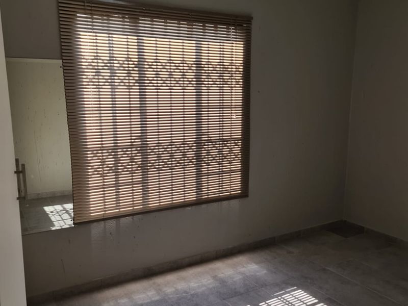 An empty bedroom featuring tiled flooring, a window with venetian blinds, and a security gate, offering a neutral space ready for personalization.
