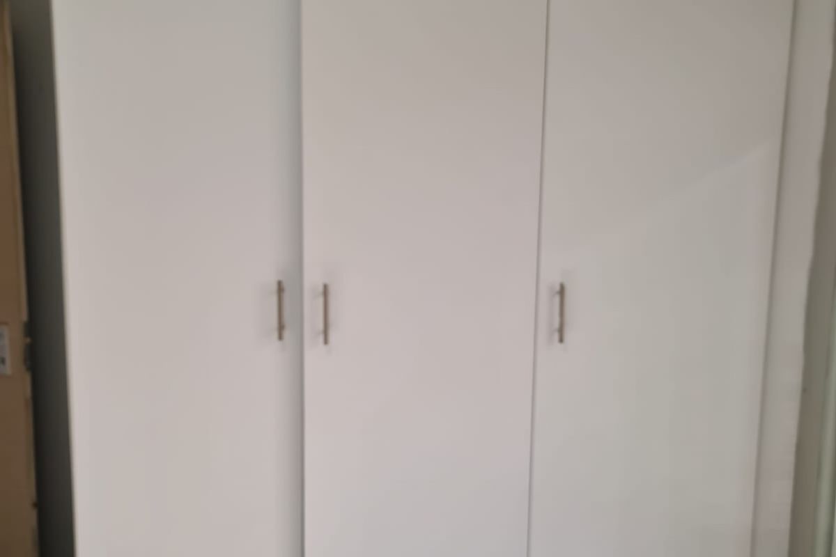 A bedroom featuring a white built-in wardrobe with three doors and modern handles.