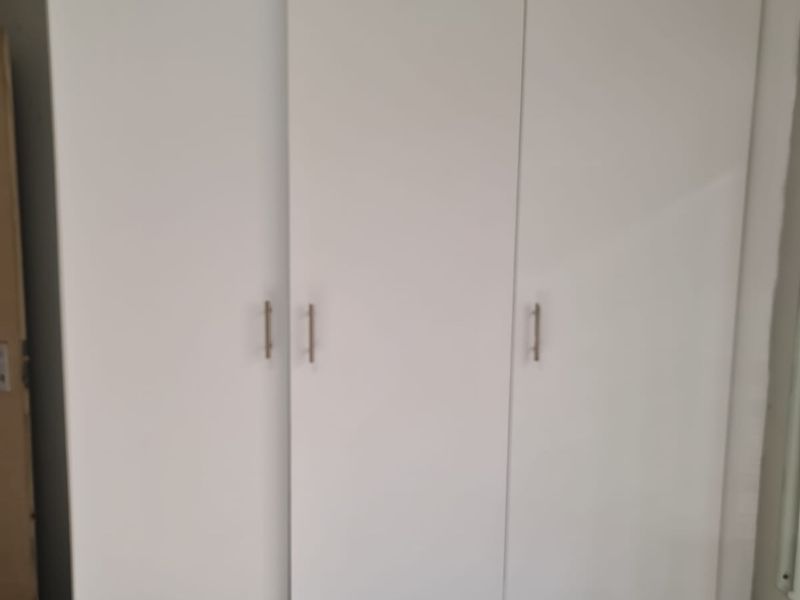 A bedroom featuring a white built-in wardrobe with three doors and modern handles.