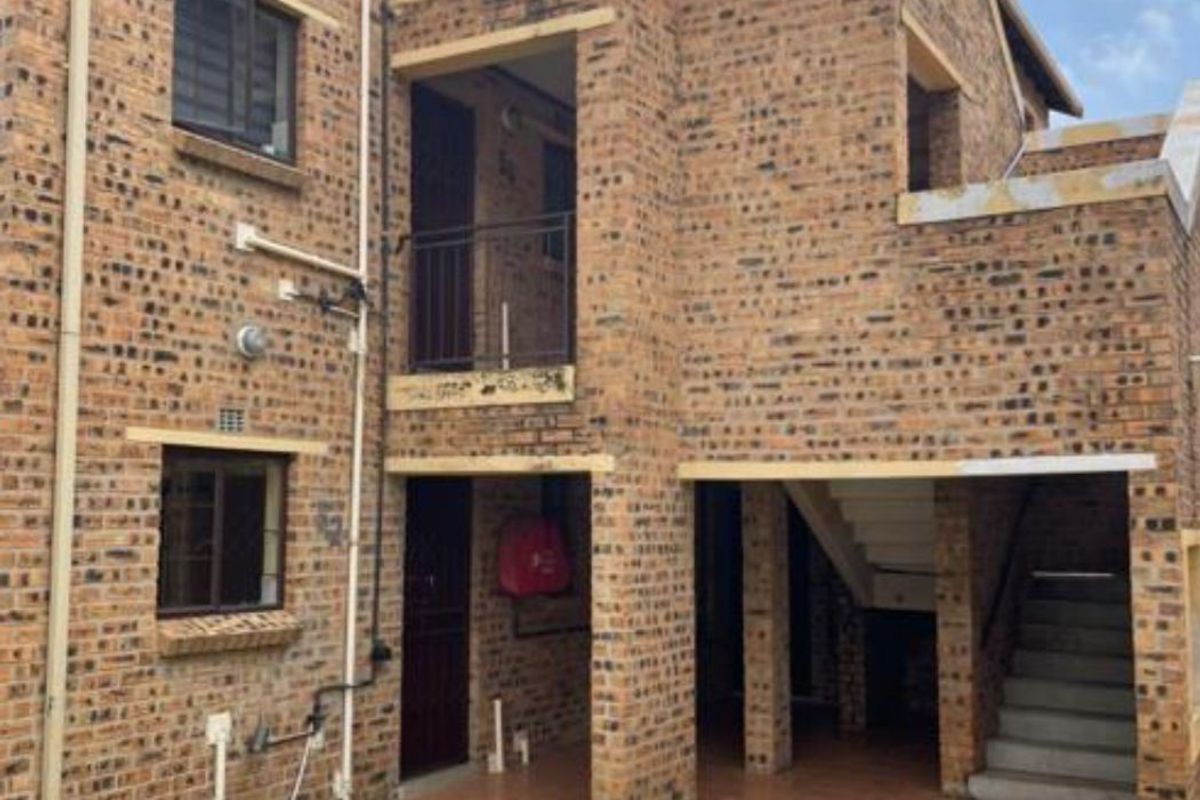 Rear view of a multi-story apartment building featuring face brick construction, private balconies, and an external staircase leading to upper levels.