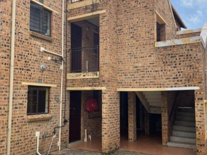 Rear view of a multi-story apartment building featuring face brick construction, private balconies, and an external staircase leading to upper levels.