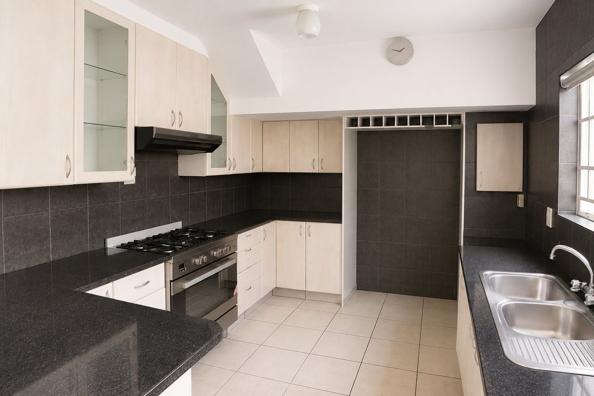 A clean, functional kitchen featuring light wood cabinetry, dark granite countertops, a gas hob, and a double stainless steel sink.