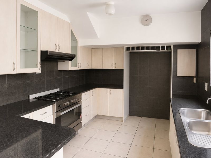 A clean, functional kitchen featuring light wood cabinetry, dark granite countertops, a gas hob, and a double stainless steel sink.